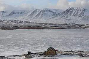 An isolated holiday home in a snow-covered landscape against an impressive mountain backdrop