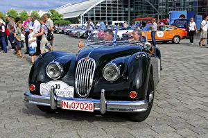 Jaguar XK 140, black convertible with two men at an open-air classic car event