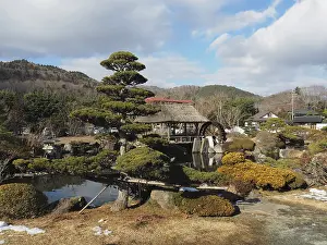 Japanese garden with traditional house and well-kept trees against mountain backdrop