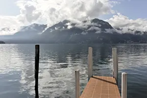 A jetty stretches into a quiet lake with mountains in the background