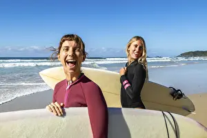 Two joyful female surfers standing on a sandy beach holding surfboards