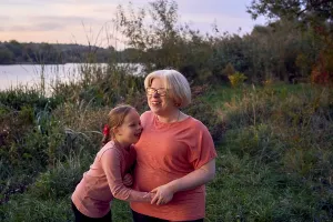 A joyful mother and daughter share a laugh in a serene outdoor setting by the riverside at sunset