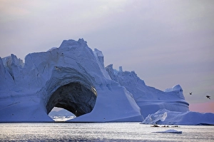 Kayaks in front of huge iceberg with cave