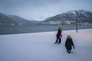 Kids walking in a deep snow in front of waters of a fiord