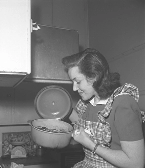 In the kitchen 1940s. Interior of a kitchen and a young woman lifting the lid of a saucepan steaming hot and looks happy with how it turned out. Sweden 1946 Kristoffersson ref CC122-1