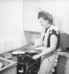 In the kitchen 1940s. Interior of a kitchen and a young woman standing at the kitchen cooker frying eggs in the frying pan. She is wearing a apron. Sweden 1947. Kristoffersson ref AB3-2