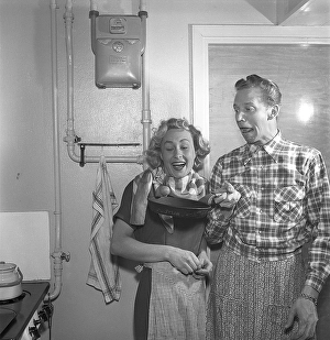 In the kitchen in the 1950s. Ayoung couple in the kitchen playing around with something in a frying pan