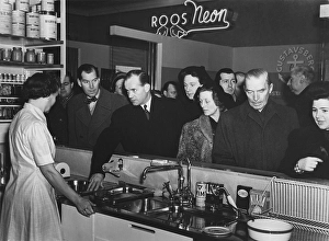 Kitchen of the 1950s. An exhibition at a public consumer fair is going on and visitors at the display of a modern kitchen are interested to know more. A woman in the stand answers questions