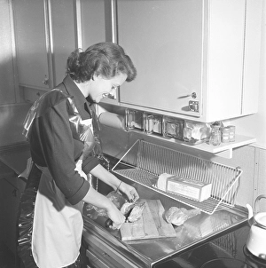 In the kitchen 1950s. Interior of a kitchen and a young woman standing at the kitchen sink preparing the ingredients