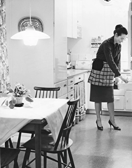 In the kitchen 1960s. Interior of a kitchen and a women taking something from a kitchen drawer