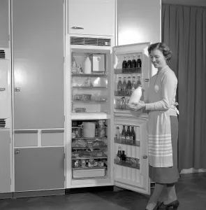 In the kitchen 1960s. A woman in her kitchen with the door open to the the refrigerator