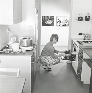 In the kitchen in the 1960s. A young woman in the kitchen taking out the ready baked breads from the oven