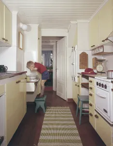 Kitchen of the 50s-60s. A boy is standing on a footstool and washes his hands and face