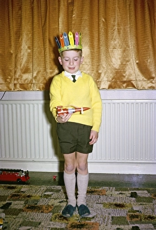 Kleiner Junge mit gelbem Pullover und rotem Indianerhut spielt am Weihnachtsmorgen mit einer roten Weltraumrakete, britische Kultur 1967