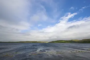 A lake with blue sky and clouds surrounded by green hills
