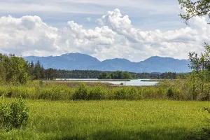 A lake with grassy meadows and mountains in the background under a cloudy sky