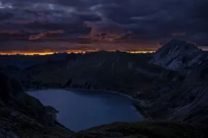 Lake Luener See with Montafon mountains and dramatic cloudy sky at sunrise