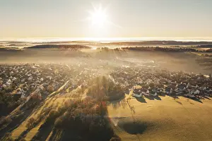 Landscape with settlement in warm light of sunrise and fog