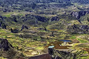 Landscape with terraced fields surrounded by mountains and a small lake under cloudy sky