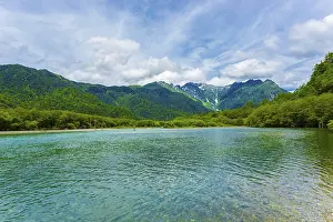 Landscape of turquoise water of Taisho Pond shoreline with nature view of Mount Hotaka Dake in background on a summer