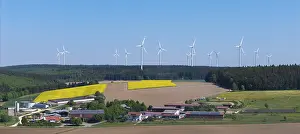 Landscape with wind turbines above agricultural fields and farms in front of a blue sky