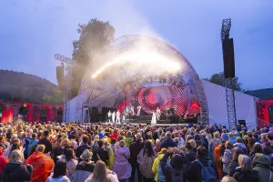 A large crowd in front of a brightly lit stage at an open-air evening event