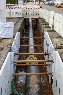 Large district heating pipeline runs through a construction site trench with stabilising wooden beams
