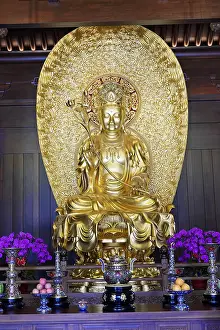 A large golden Buddha statue flanked by flowers in a temple