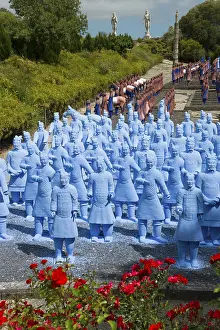 A large number of blue terracotta soldier statues stand on a path lined with flowers