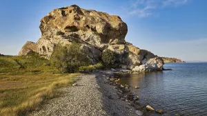 Large rock formation on the coast with clear sky and grassy areas in the foreground