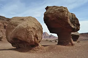 Two large rocks stand side by side in a desert landscape with a red rock backdrop