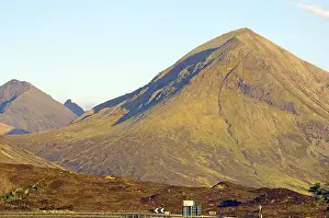 Large single mountain with rocky surface illuminated by yellow sunlight under a clear blue sky