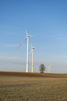 Three large wind turbines stand in a green landscape under a blue sky