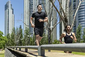 Two latin men running in a park surrounded by modern skyscrapers