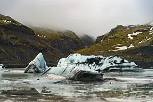 Layers of icebergs against a backdrop of towering mist-covered mountains