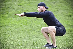 Full length of young concentrated sportsman doing squats outdoors
