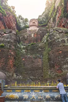 Leshan, China - July 2019 : Chinese male pilgrim lightening memorial candles at the bottom of The Giant Leshan Buddha