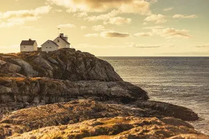 A lighthouse and house on rocky cliffs by the ocean at sunset
