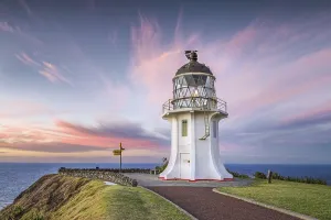 Lighthouse with signpost at Cape Reinga at sunset with pink clouds