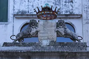 Two lion sculptures with a coat of arms and crown in front of a palazzo