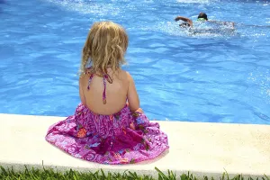 Little blond girl sitting rear back swimming pool outdoor