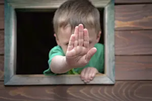 Little Caucasian boy looking through the window of a wooden toy house in a outdoor playground