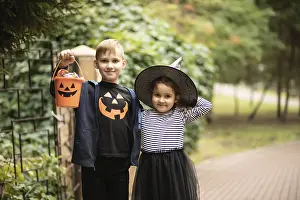 Little cute girl in witch costume and boy holding jack-o-lantern pumpkin bucket with candies and sweets