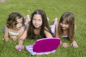 Three little girl outdoor playing with toy computer in grass