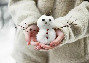 Little snowman, decorated with twigs and berries, held in children's hands in a winter garden with lots of snow. Winter atmosphere