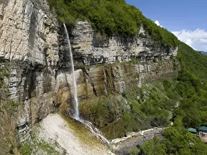 Long waterfall falls over a rock face into a wooded area under a clear sky