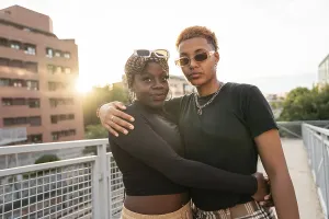 A loving LGBT multiethnic couple embraces outdoors on a bridge during a beautiful sunset