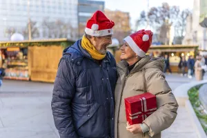 Loving senior couple wearing santa hats exchanging christmas gifts at a christmas market in the city