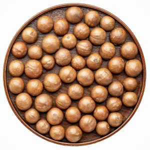 Macadamia nuts in shells on on a round wooden tray isolated on white