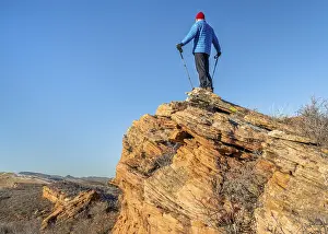 Male hiker with trekking poles on a sandstone cliff against blue sky